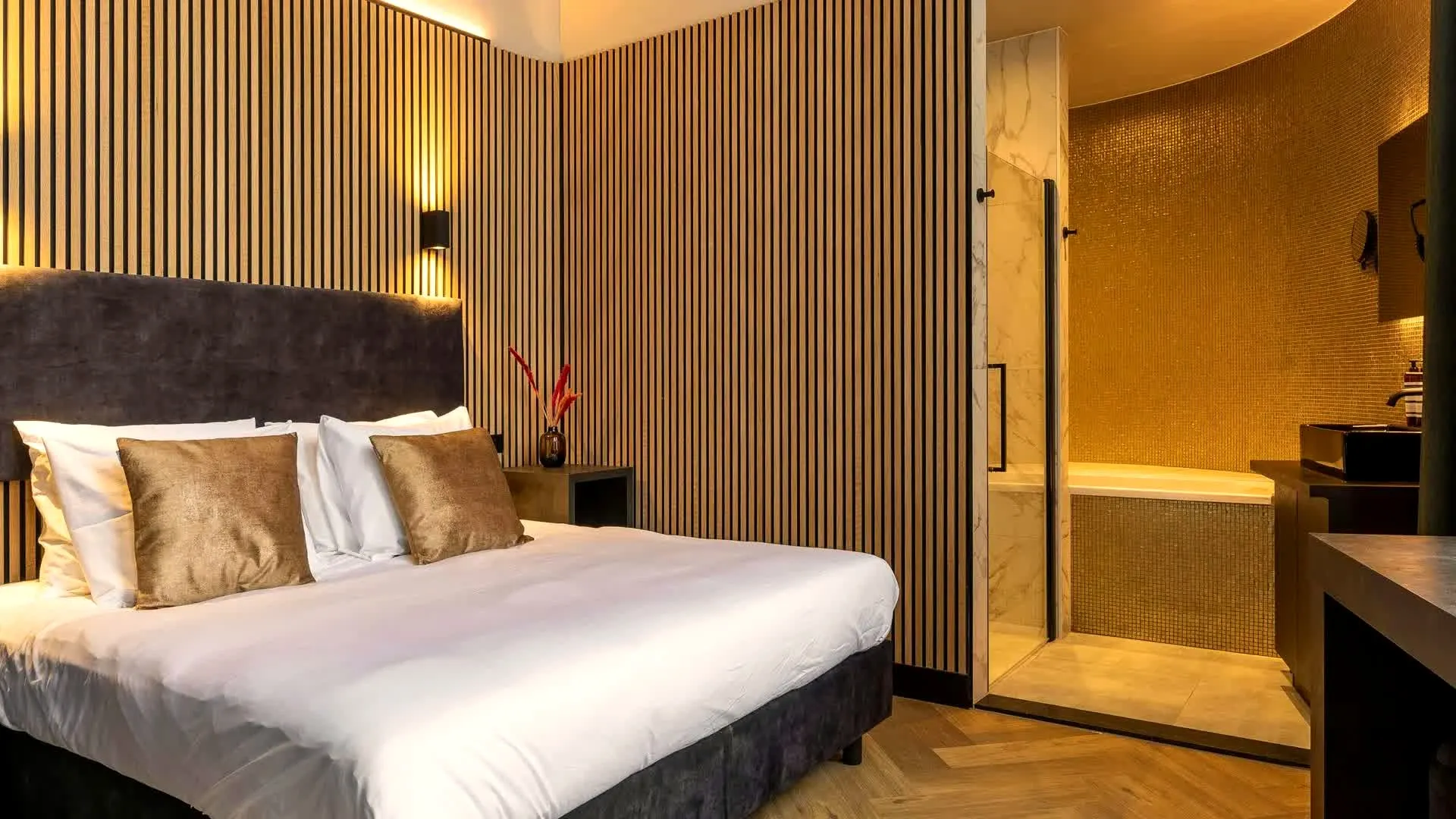 Hotelkamer met houten lamellenwand en een open badkamer met gouden mozaïek